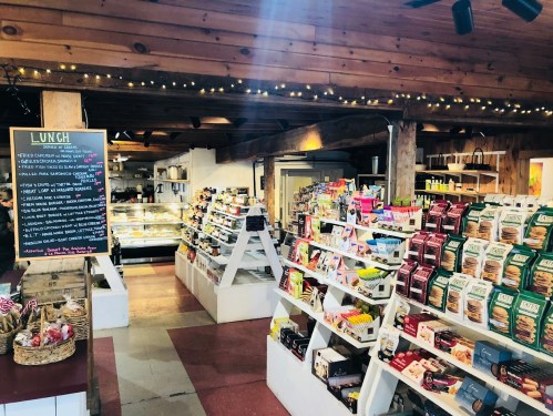A cozy market interior with shelves of snacks, a lunch menu board, and warm lighting.