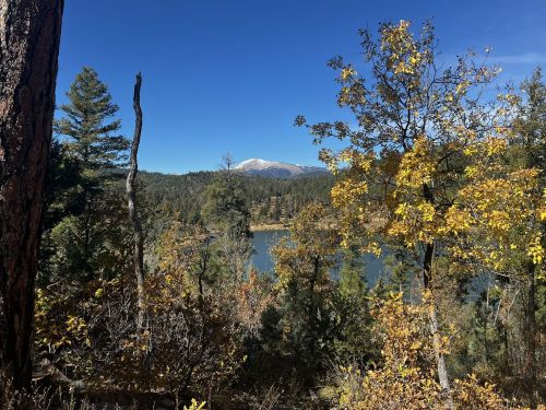 Scenic view of a lake surrounded by autumn trees and mountains under a clear blue sky.