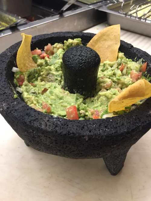 A traditional stone mortar filled with fresh guacamole, garnished with tortilla chips and diced tomatoes.