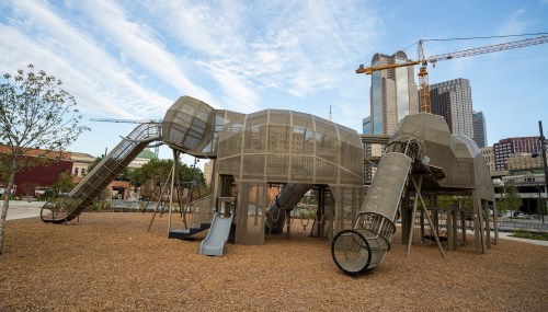 A large, modern playground structure resembling an elephant, with slides and tunnels, set against a city skyline.