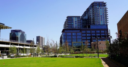 A modern urban landscape featuring green space, tall buildings, and clear blue skies.