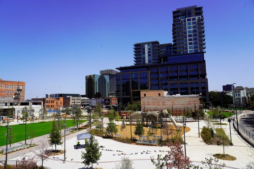 A modern urban park with playground equipment, surrounded by buildings and clear blue skies.