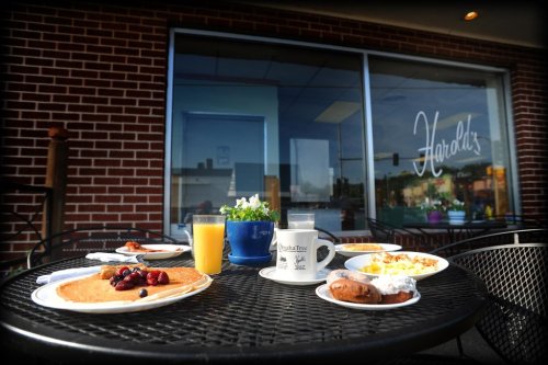 A table set with pancakes, eggs, orange juice, and coffee outside Harold's restaurant, with a flower pot in the background.