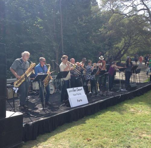 A jazz band performs on stage outdoors, featuring various musicians with instruments like saxophones and trumpets.