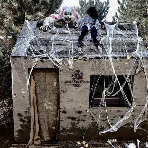 A creepy, abandoned house covered in cobwebs, with a spooky figure and a mannequin on the roof.