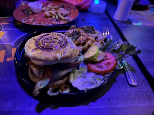 A plate featuring a burger with lettuce, tomato, and a side of greens, served on a colorful table.