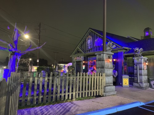 A spooky-themed restaurant with eerie decorations, a picket fence, and a foggy night sky.