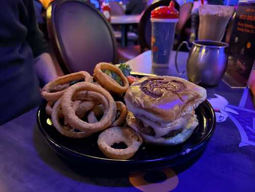 A plate with a burger and a side of onion rings, set in a dimly lit restaurant with colorful lighting.