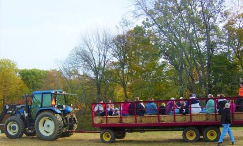 A tractor pulls a hayride filled with people through a colorful autumn landscape.