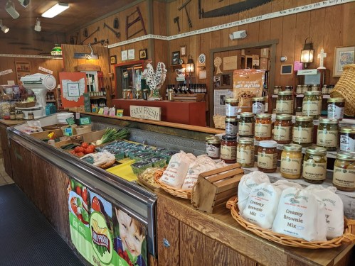 A rustic market interior featuring fresh produce, jars of preserves, and a welcoming counter with wooden decor.