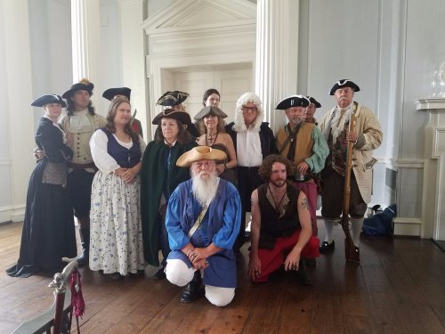 A group of people in historical costumes, including pirates and colonial attire, posing together indoors.