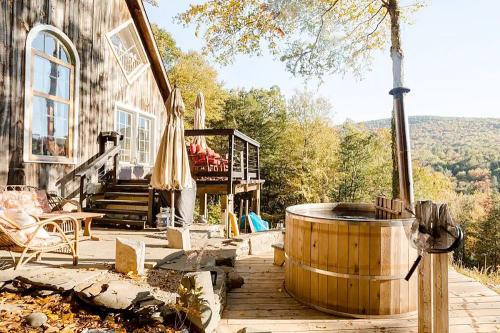 A wooden hot tub on a deck beside a rustic cabin, surrounded by autumn trees and mountains in the background.