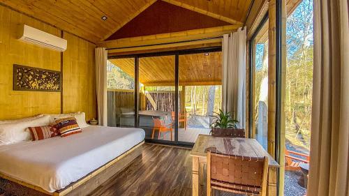 Cozy cabin interior with a bed, wooden decor, and large windows overlooking a natural setting.