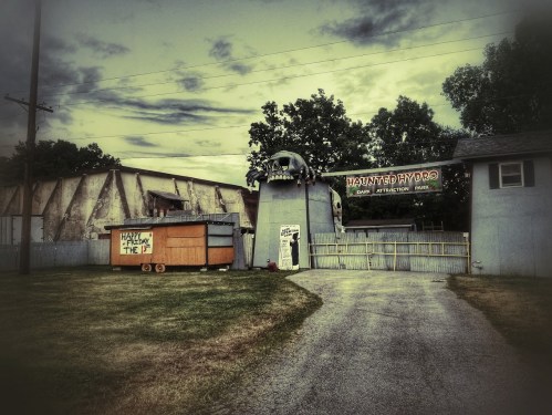 Abandoned haunted attraction with eerie signage and a rundown exterior, set against a gloomy sky.