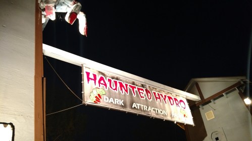 Sign for "Haunted Hydro" dark attraction, illuminated at night, with a spooky figure above.