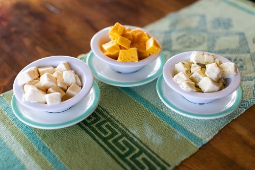 Three small bowls of cubed cheese in yellow, white, and cream colors, arranged on a green patterned tablecloth.