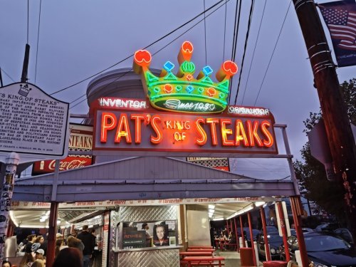 Neon sign for Pat's King of Steaks, a famous steak shop, illuminated at dusk with a crown design above the name.