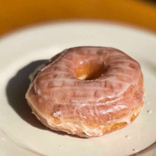 A glazed pink donut on a white plate, with a soft, shiny surface and a round shape.