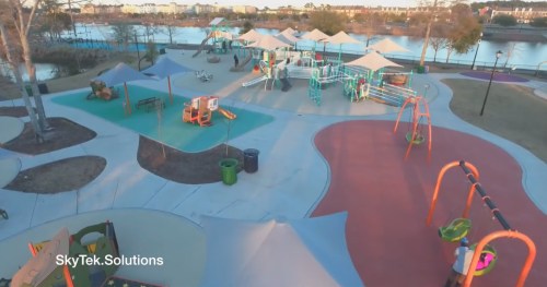 Aerial view of a colorful playground with swings, slides, and play structures near a lake.