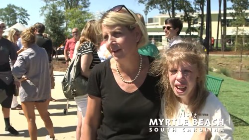 A woman and a girl stand together outdoors, surrounded by a crowd, with a sunny atmosphere in Myrtle Beach, SC.