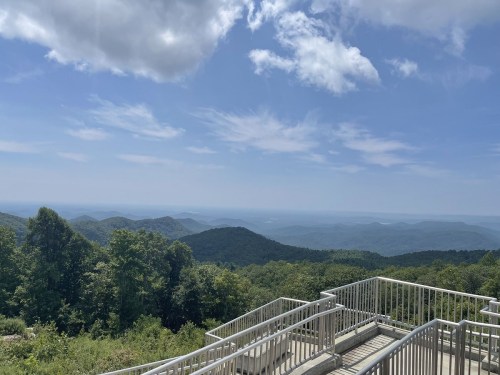 A scenic view of rolling mountains under a blue sky with fluffy clouds, seen from a lookout point.