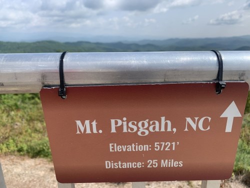 Sign for Mt. Pisgah, NC, indicating an elevation of 5721 feet and a distance of 25 miles. Scenic mountain view in background.