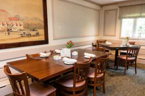 A cozy dining room with wooden tables, chairs, and a floral centerpiece, featuring a vintage mural on the wall.