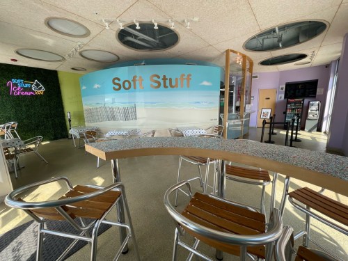 Interior of a modern ice cream shop with a colorful mural, seating, and a counter displaying soft serve options.