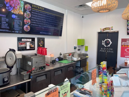 Interior of a poke restaurant featuring a menu board, food prep area, and a door labeled "Aloha."
