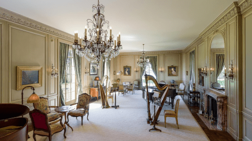 Elegant room with chandeliers, vintage furniture, and artwork, featuring a harp and a cozy fireplace.