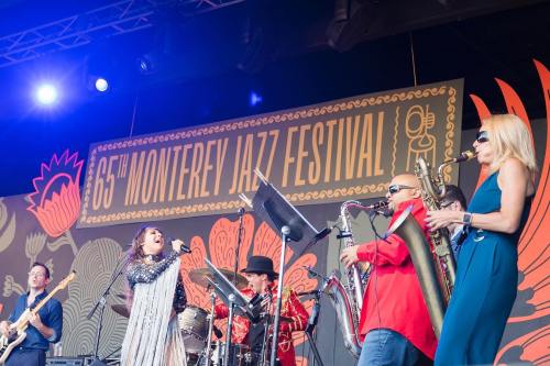 A lively jazz band performs on stage at the 65th Monterey Jazz Festival, featuring singers and musicians with instruments.