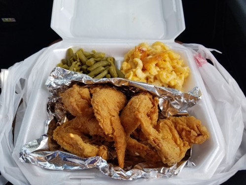 A takeout container with fried chicken wings, green beans, and macaroni and cheese.