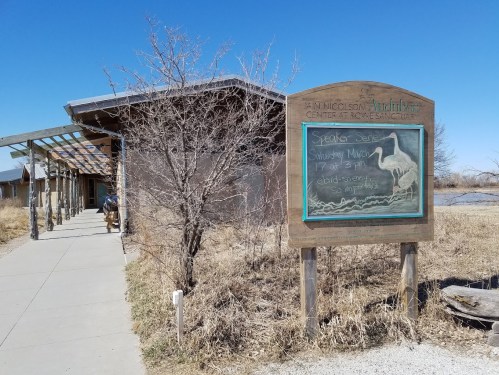 A building with a sign about a speaker event, surrounded by dry grass and a clear blue sky.