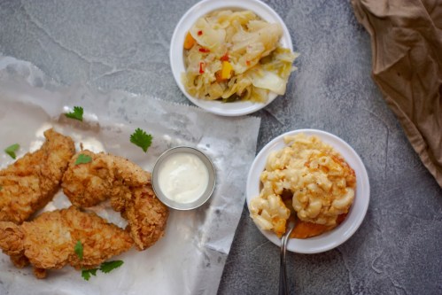 A plate of crispy fried chicken with sides of coleslaw and macaroni and cheese on a textured gray surface.