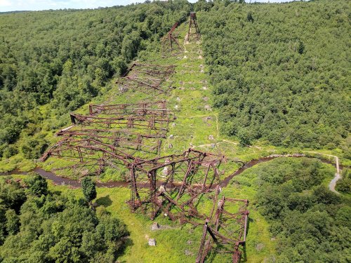 Aerial view of rusted metal structures overgrown with greenery, set in a lush, wooded landscape.