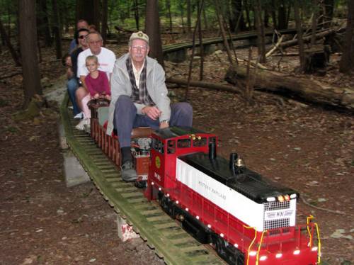 A small group of people rides on a miniature train through a wooded area, enjoying a scenic outing.
