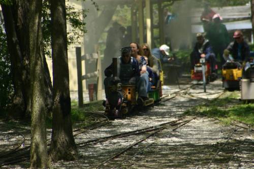 A miniature train rides along a track through a wooded area, with passengers enjoying the scenic journey.