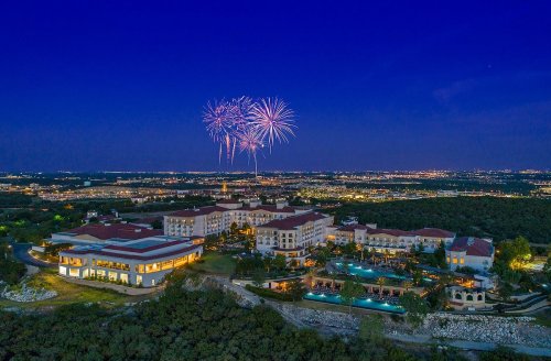 Aerial view of a resort at night with fireworks in the sky and city lights in the background.