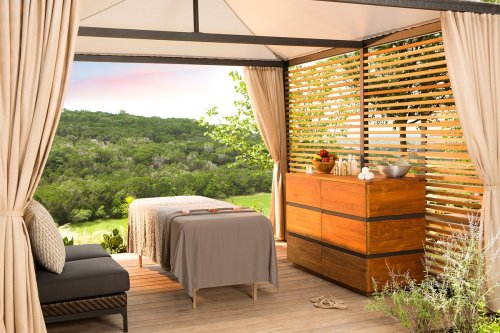 A serene outdoor spa setting with a massage table, wooden storage, and lush greenery in the background.