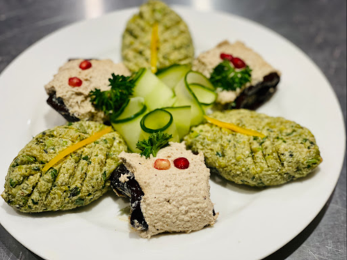 A plate of decorative green and beige appetizers, garnished with cucumber slices and herbs.