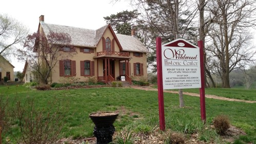 Historic Wildwood Center, a charming two-story house with a sign, surrounded by green grass and trees.