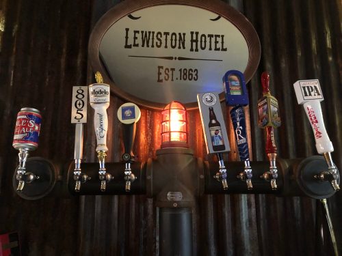 A row of beer taps featuring various brands, with a glowing light and a sign for Lewiston Hotel above.