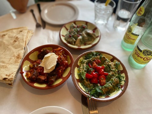 Three colorful bowls of food on a table: one with creamy dip, another with tomatoes, and a third with a savory dish.