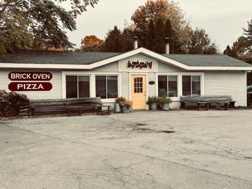 A cozy pizza restaurant with a sign reading "Brick Oven Pizza," surrounded by trees and benches.