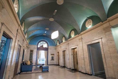 Elegant lobby with arched ceilings, decorative lighting, and marble walls, featuring elevators and a seating area.