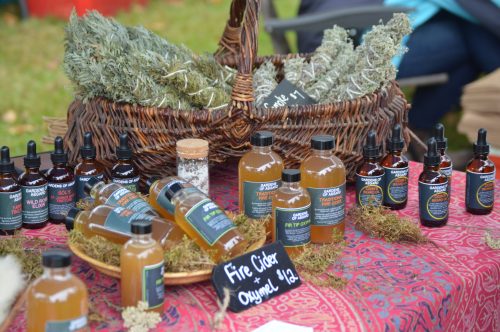 A woven basket filled with herbs and various bottles of herbal remedies displayed on a patterned tablecloth.