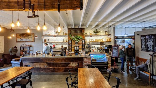 Cozy coffee shop interior with wooden tables, a rustic counter, and patrons enjoying their drinks in a warm atmosphere.