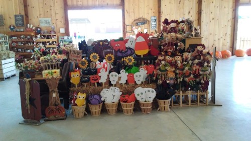 A display of colorful fall decorations, including scarecrows, pumpkins, and festive crafts in a wooden barn setting.