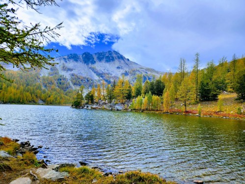 A serene lake surrounded by autumn-colored trees and mountains under a partly cloudy sky.