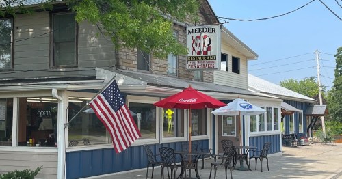 Exterior of Meeder Restaurant with outdoor seating, American flag, and a sign featuring pies and shakes.